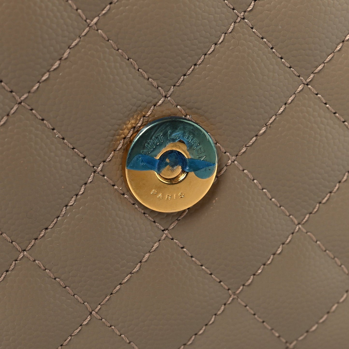 Round metal snap button on dusty grey quilted satchel front