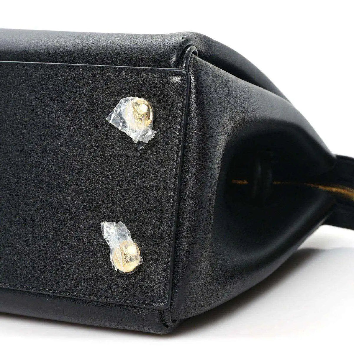 Black leather handbag corner with two gold-tone studs and stitched edge