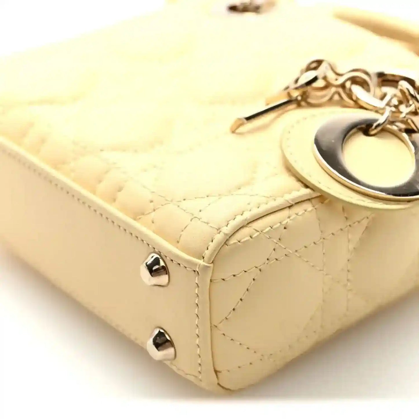 Soft yellow handbag side detail with cannage quilting, strap, and metal stud feet
