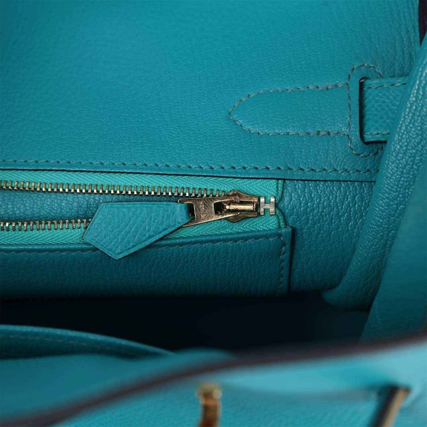 Blue peacock leather zip pocket with gold zipper pull, tab, and stitched seams