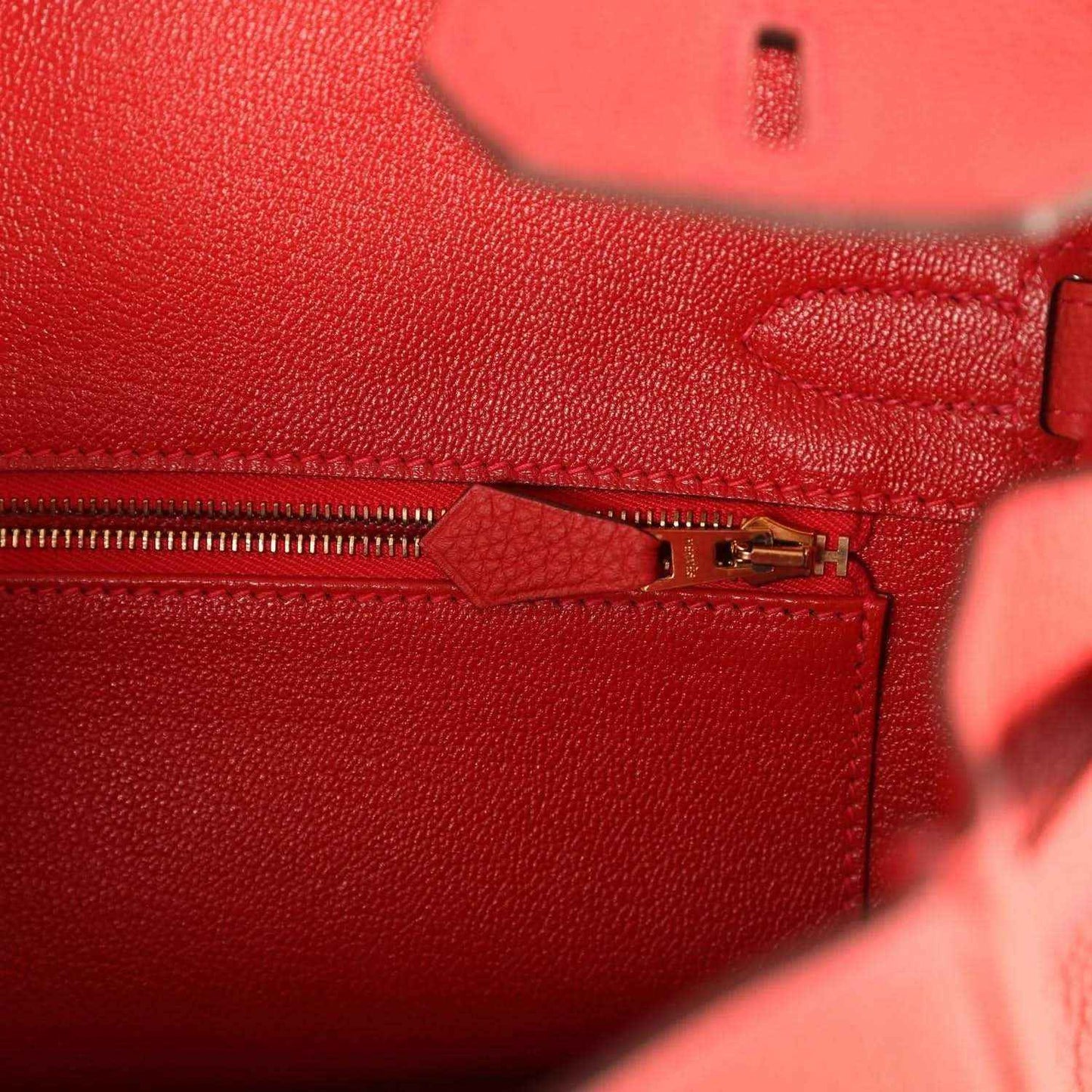 Red leather handbag close-up of gold clasp and zipper pull