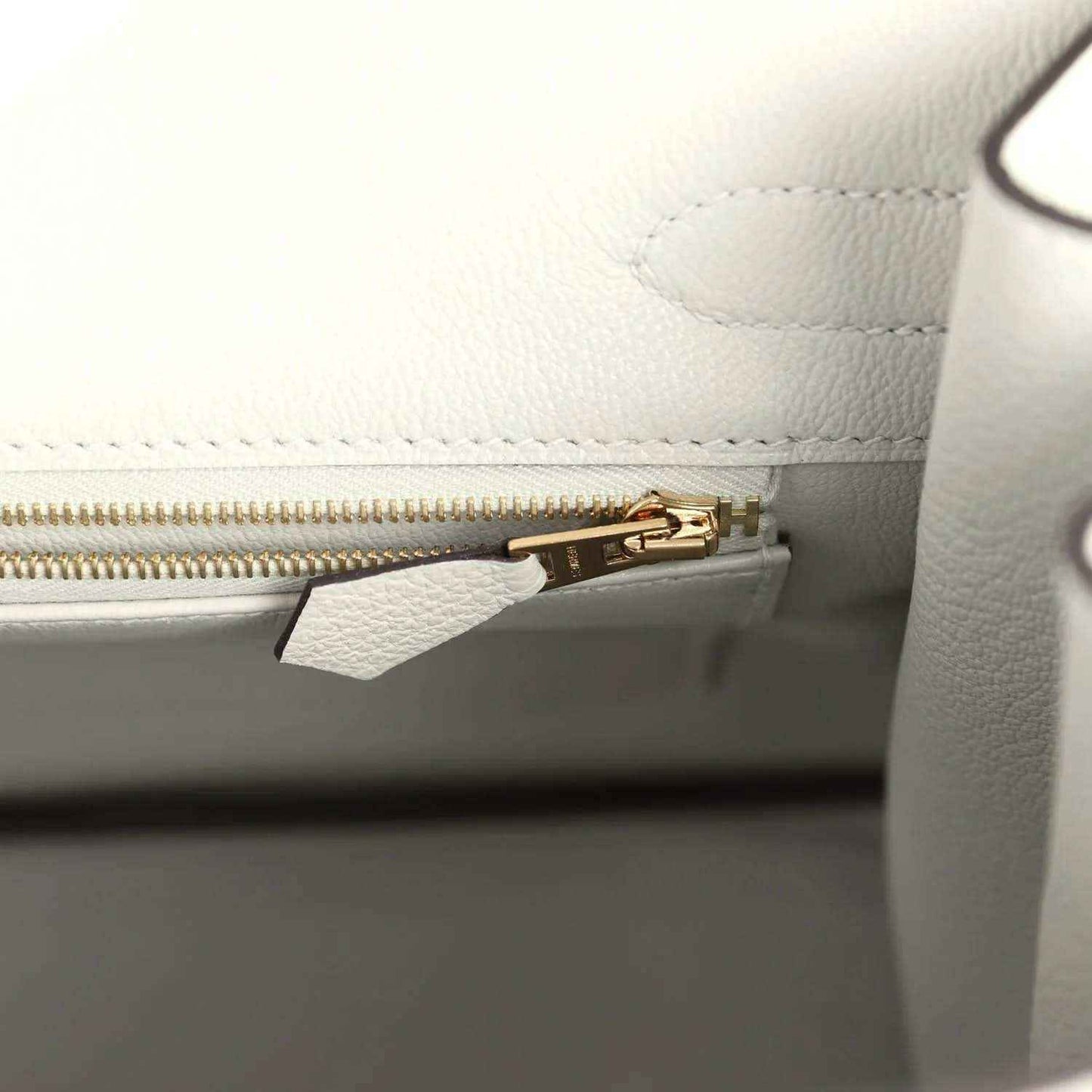 Light gray leather handbag interior with gold zipper and small hardware clip