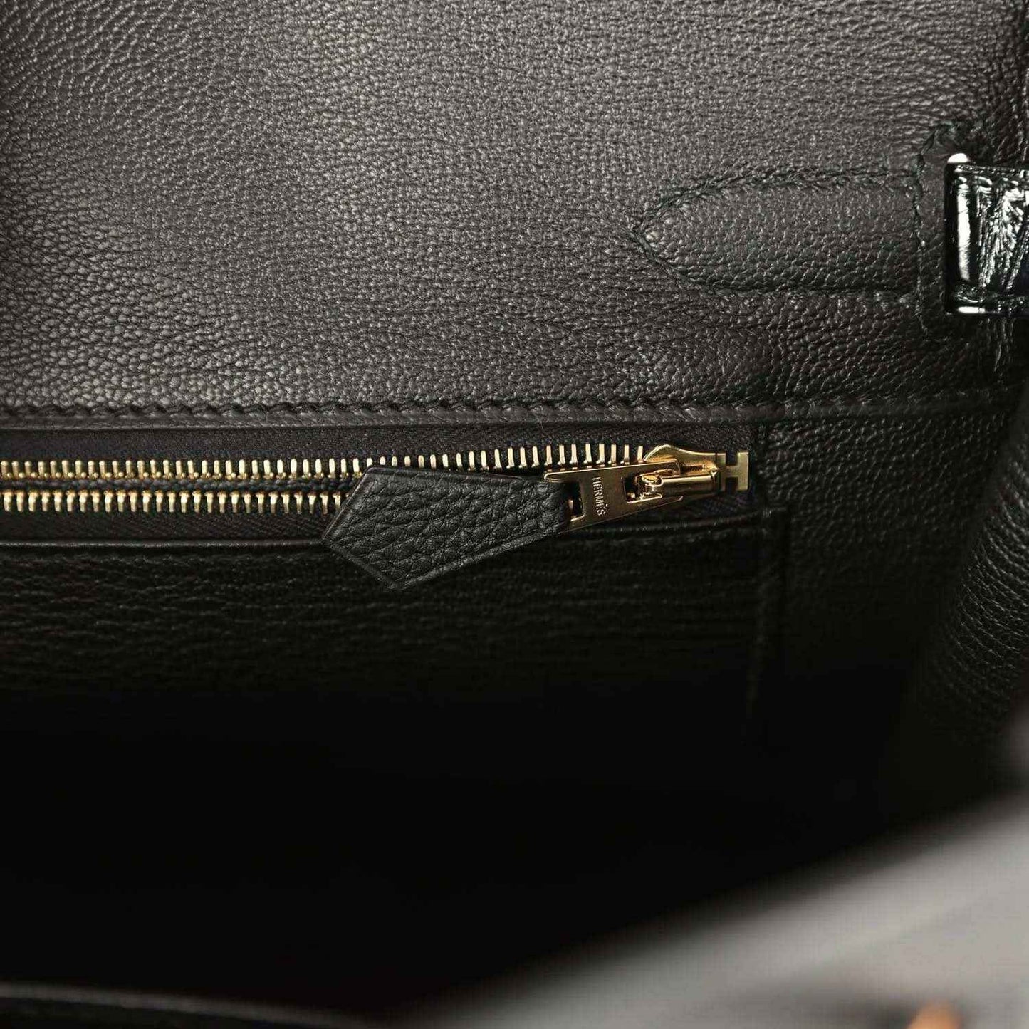 Dark green leather handbag interior with gold zipper pull and pocket seam