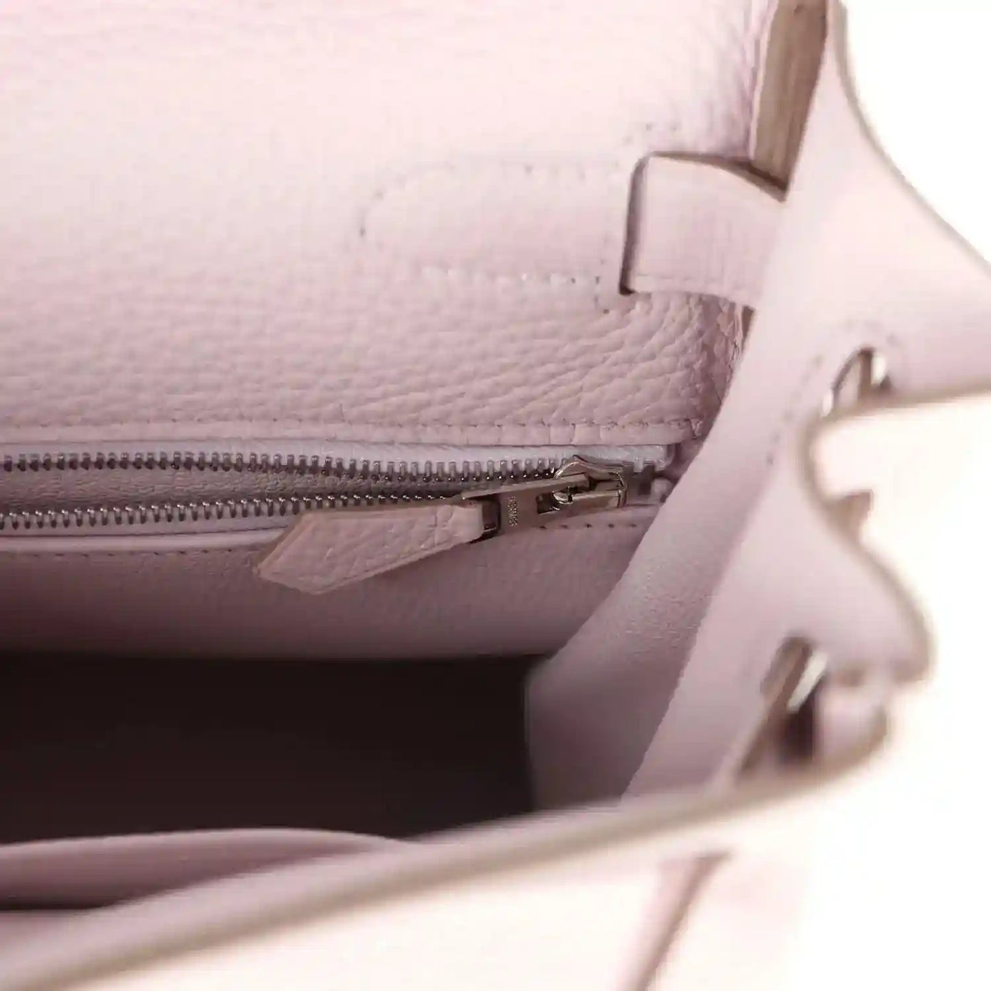 Light mauve leather handbag interior close-up with zipper track and leather divider