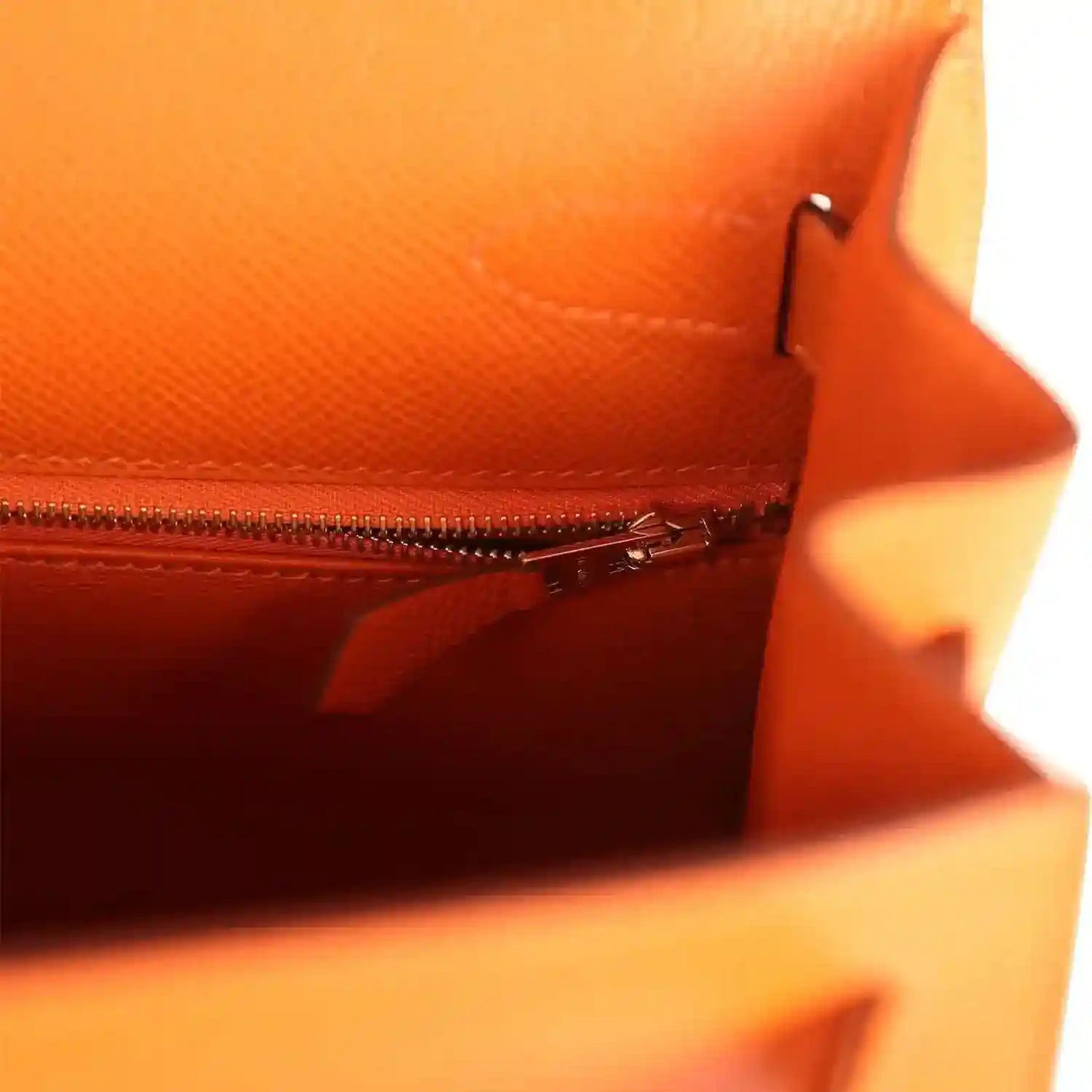 Orange leather Kelly bag interior with zip pocket and zipper pull, close-up.