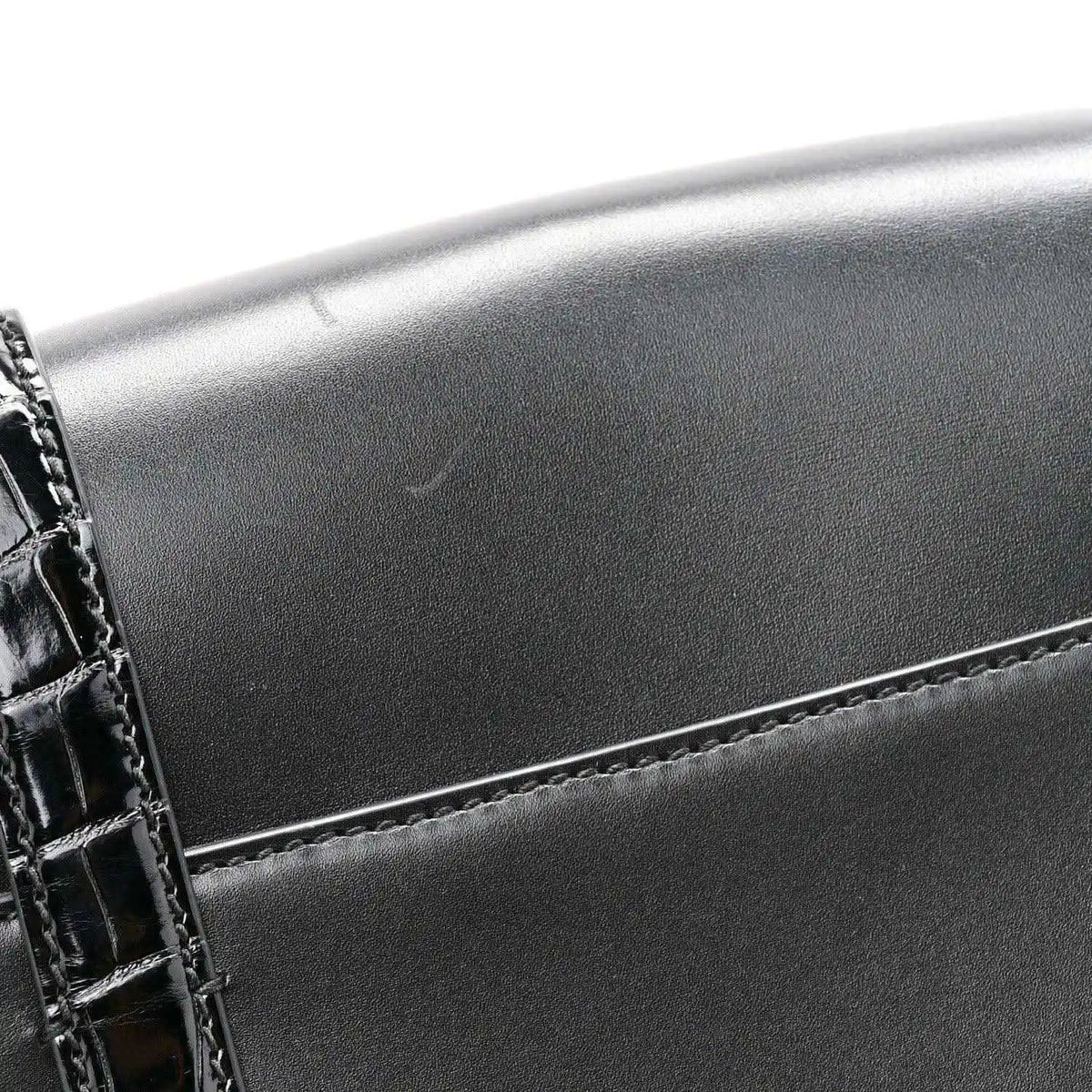 Black messenger bag corner with crocodile-embossed trim and double buckle detail