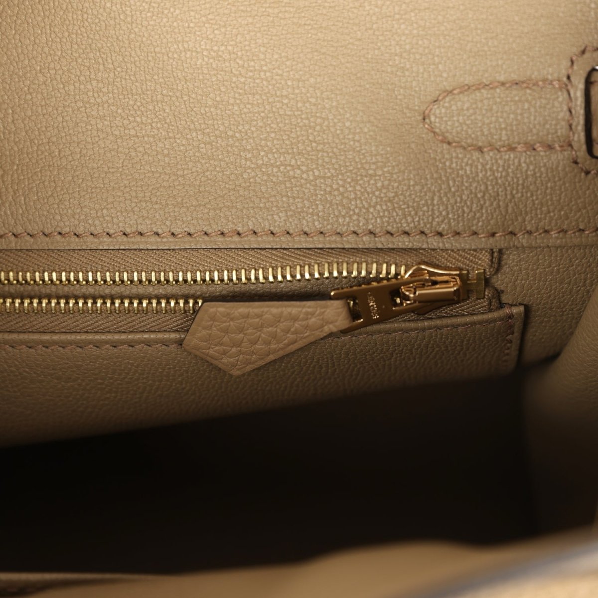 Beige leather handbag interior close-up of gold zipper and leather tab