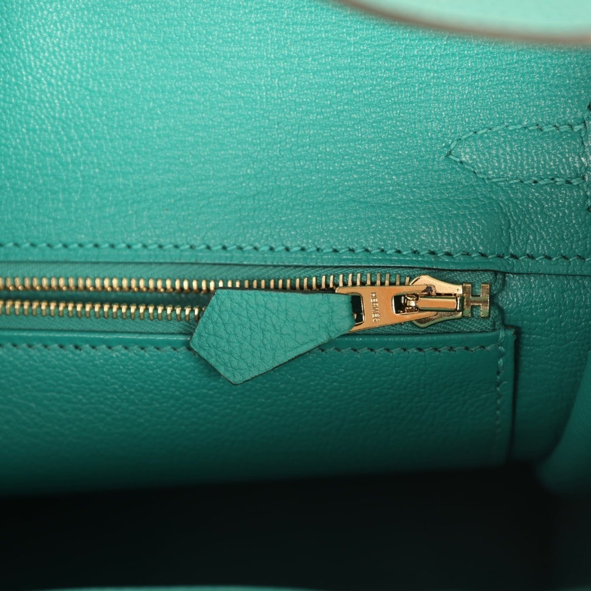 Green leather bag with gold zipper pull and stitched edge detail
