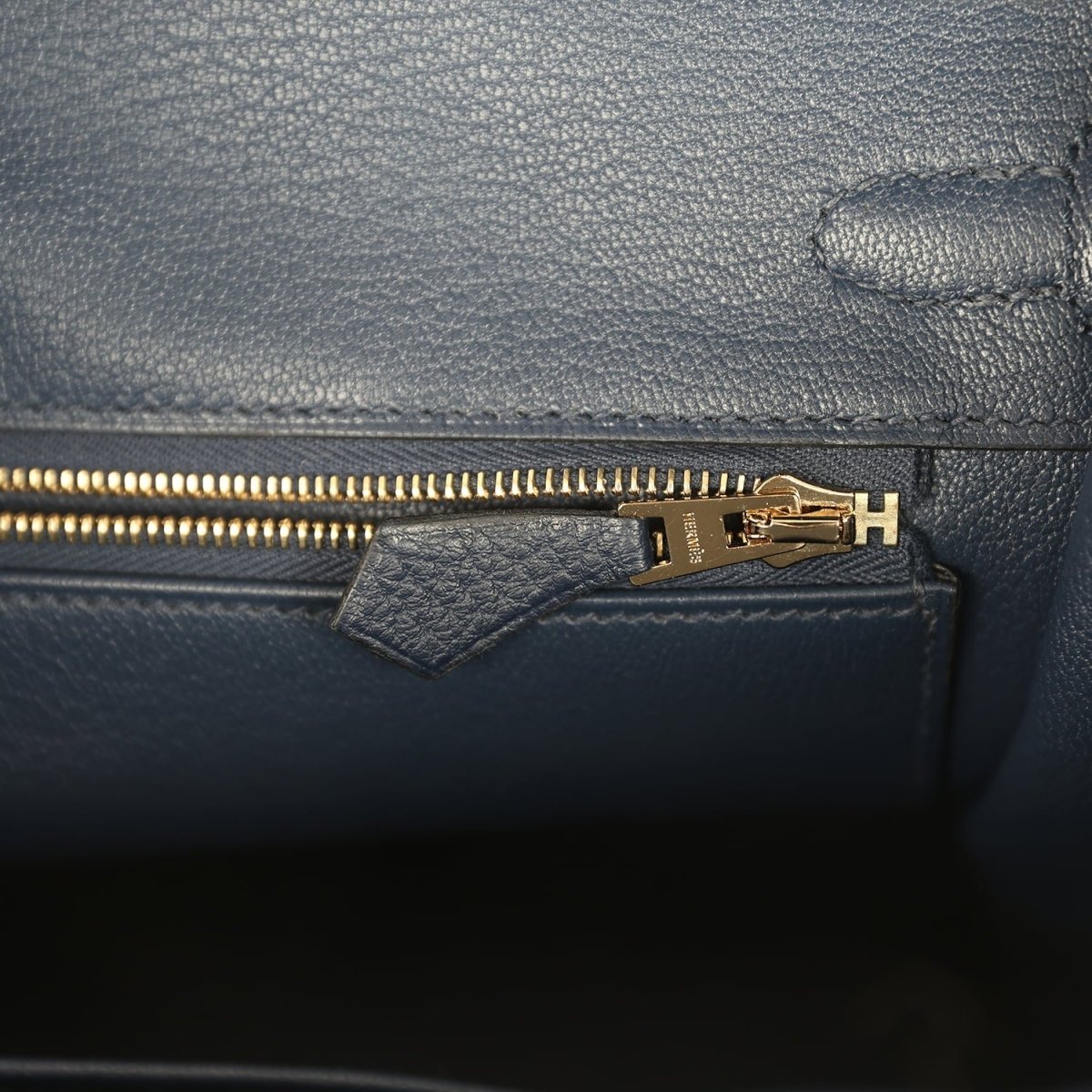 Gold zipper pull on blue Togo leather inner pocket with stamped hardware plate