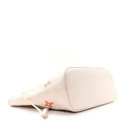 Neutral tote bag with monogram accents and top zipper pull, side view