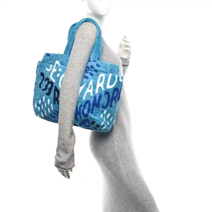 Turquoise beach tote held at side, featuring black-and-white graphic lettering on terry fabric.
