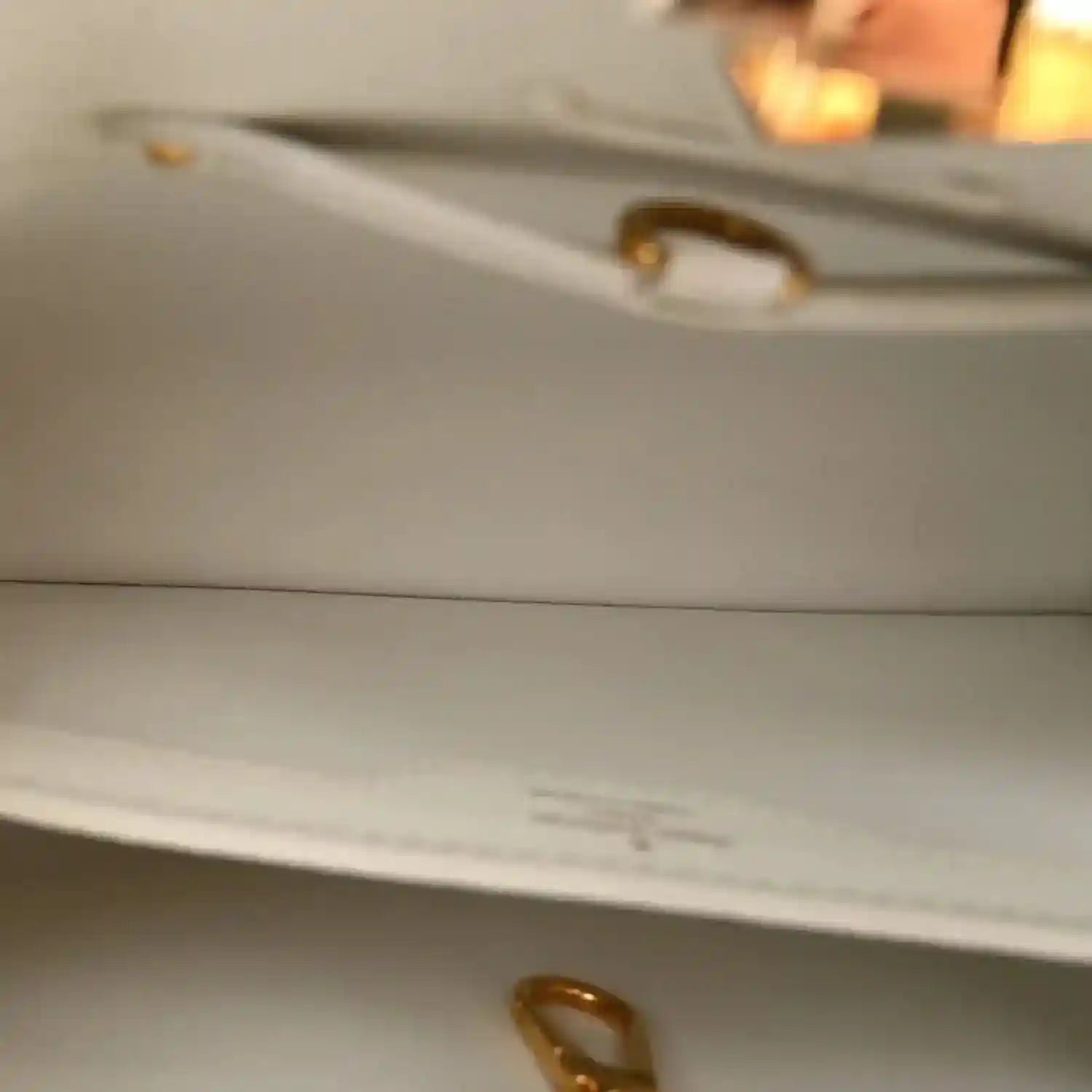 White leather bag close-up with gold handle hardware and interior edge