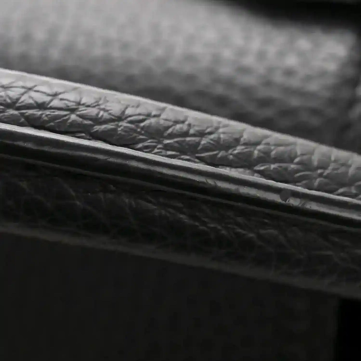 Black textured leather bag edge with gold-toned trim close-up