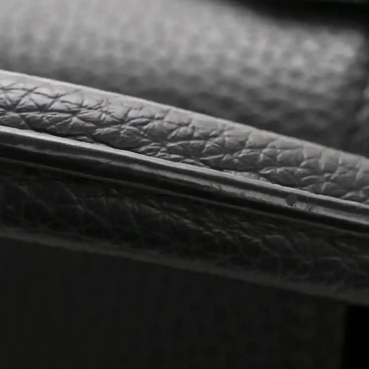 Black textured leather bag edge with gold-toned trim close-up