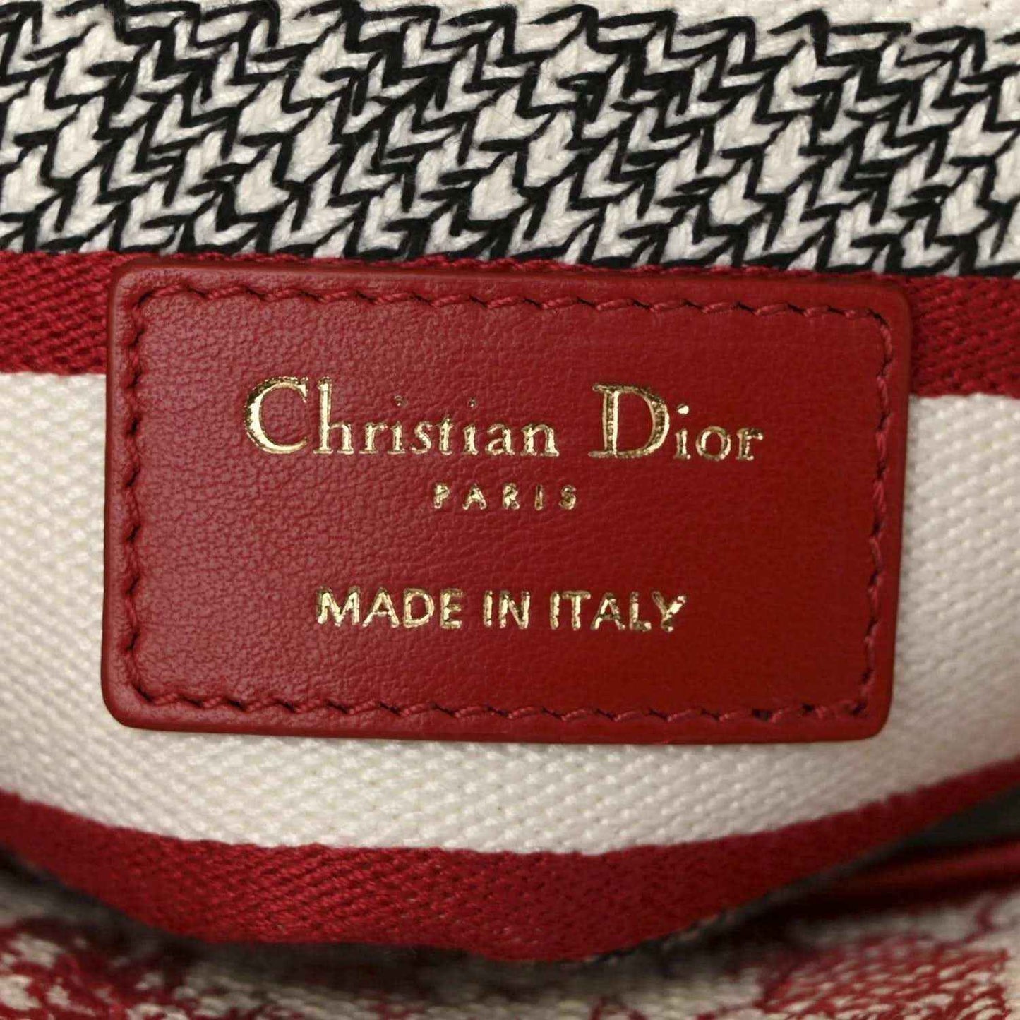 Red leather brand label on canvas bag reading Christian Dior and Made in Italy.