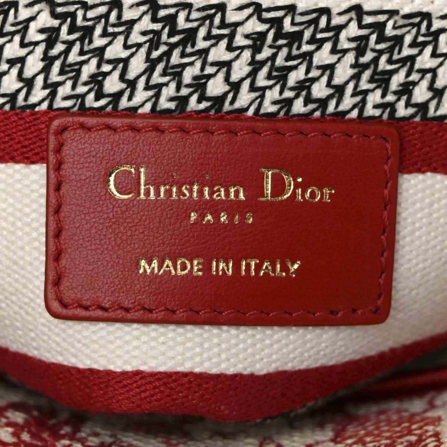 Red leather brand label on canvas bag reading Christian Dior and Made in Italy.