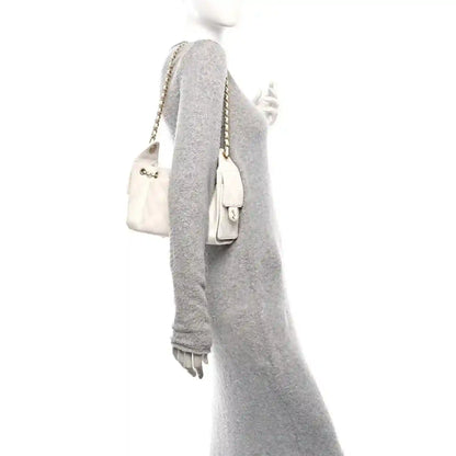 White mini quilted handbag with chain strap worn on a grey knit dress