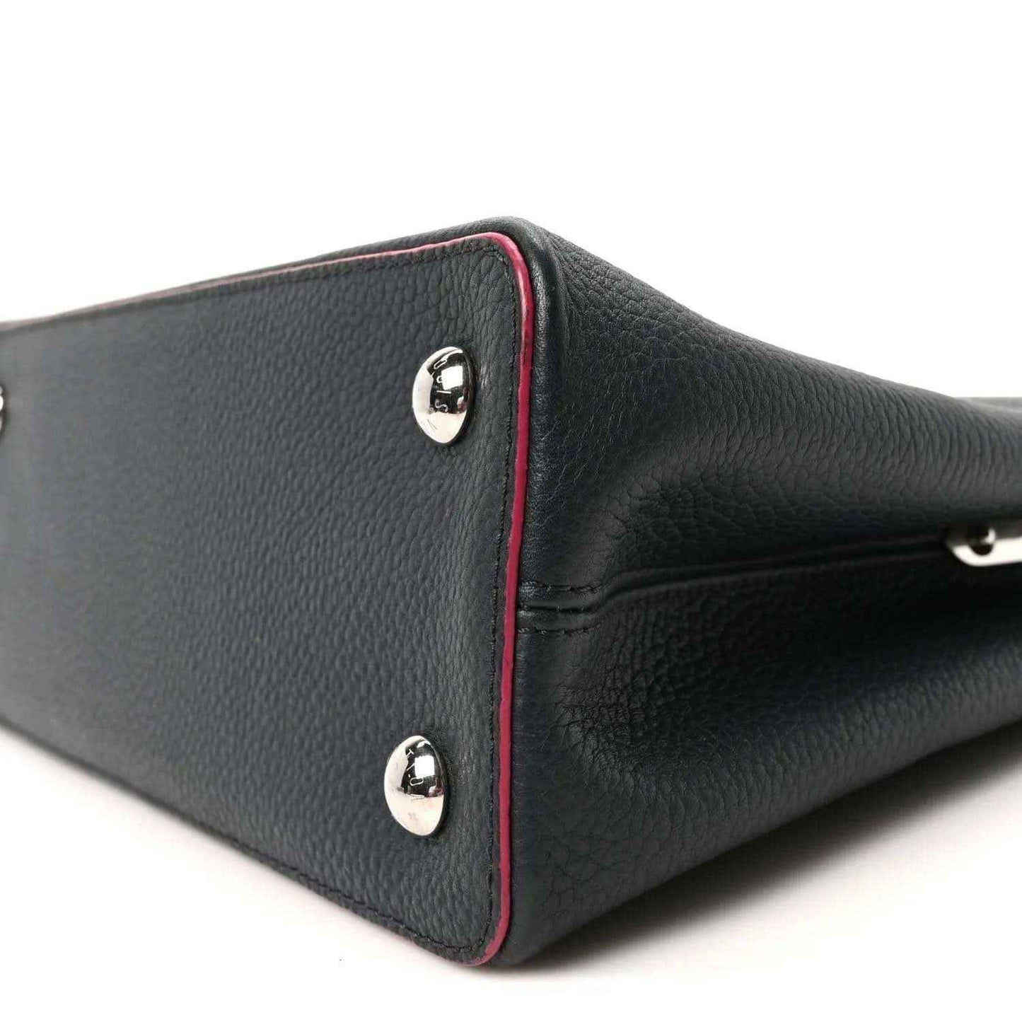 Louis Vuitton Capucines PM leather bag corner close-up, dark blue with fuchsia trim and silver studs