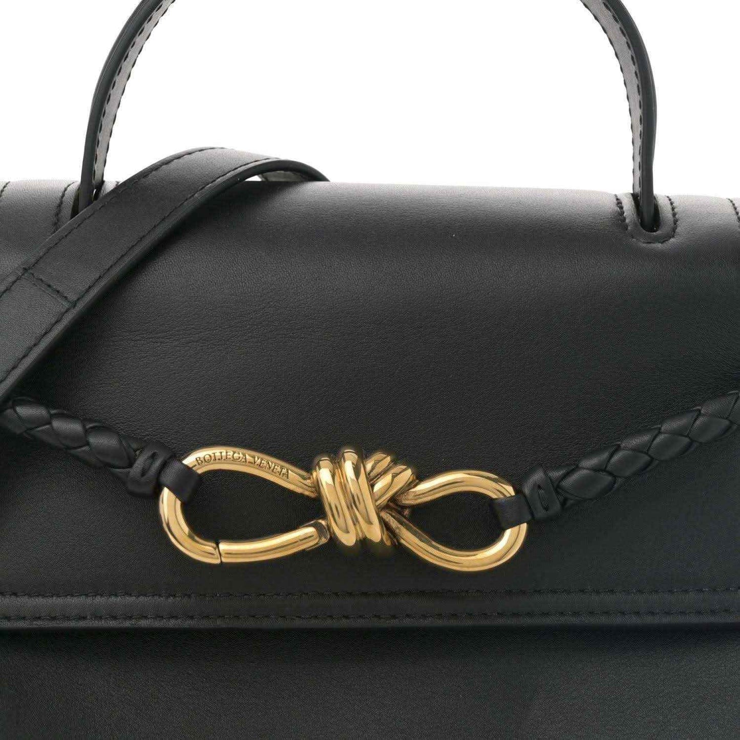 Black leather shoulder bag close-up with braided strap and gold bow clasp.