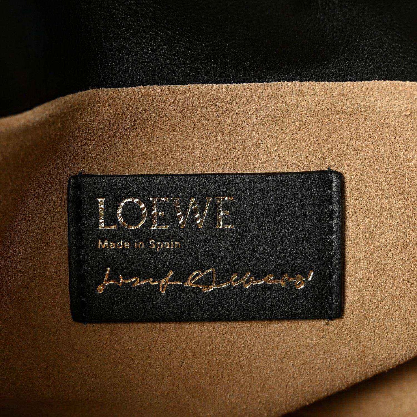 Black leather clutch label reading “LOEWE” and “Made in Spain” with signature