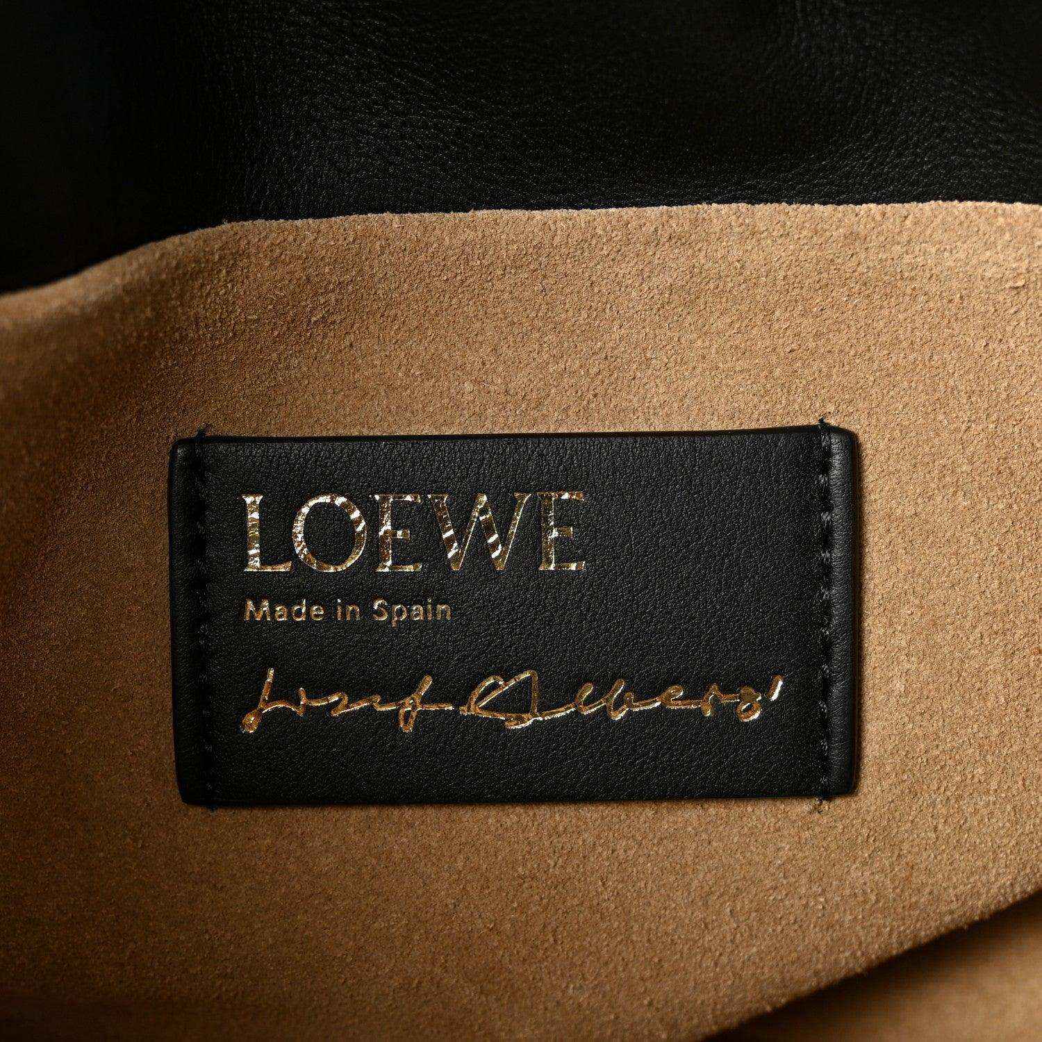 Black leather clutch label reading “LOEWE” and “Made in Spain” with signature