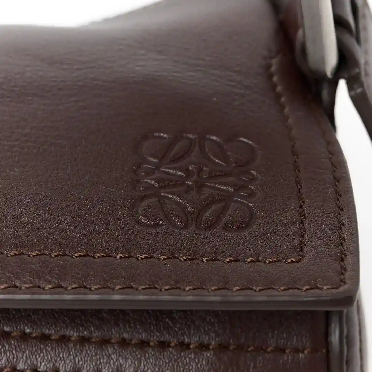 Leather corner detail of small biker bag with embossed logo and stitched edge