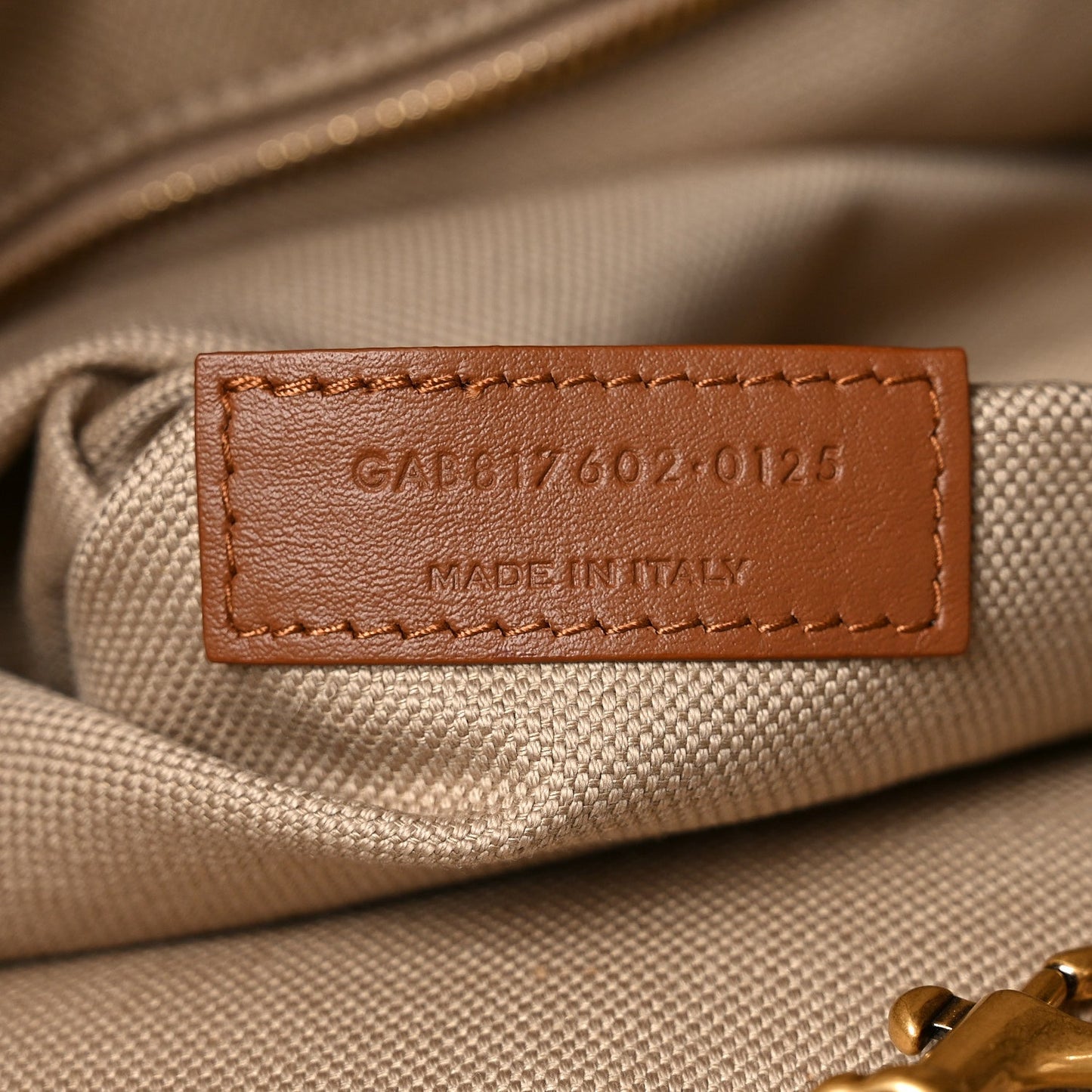 Beige interior leather label with stitched text and code on tote bag