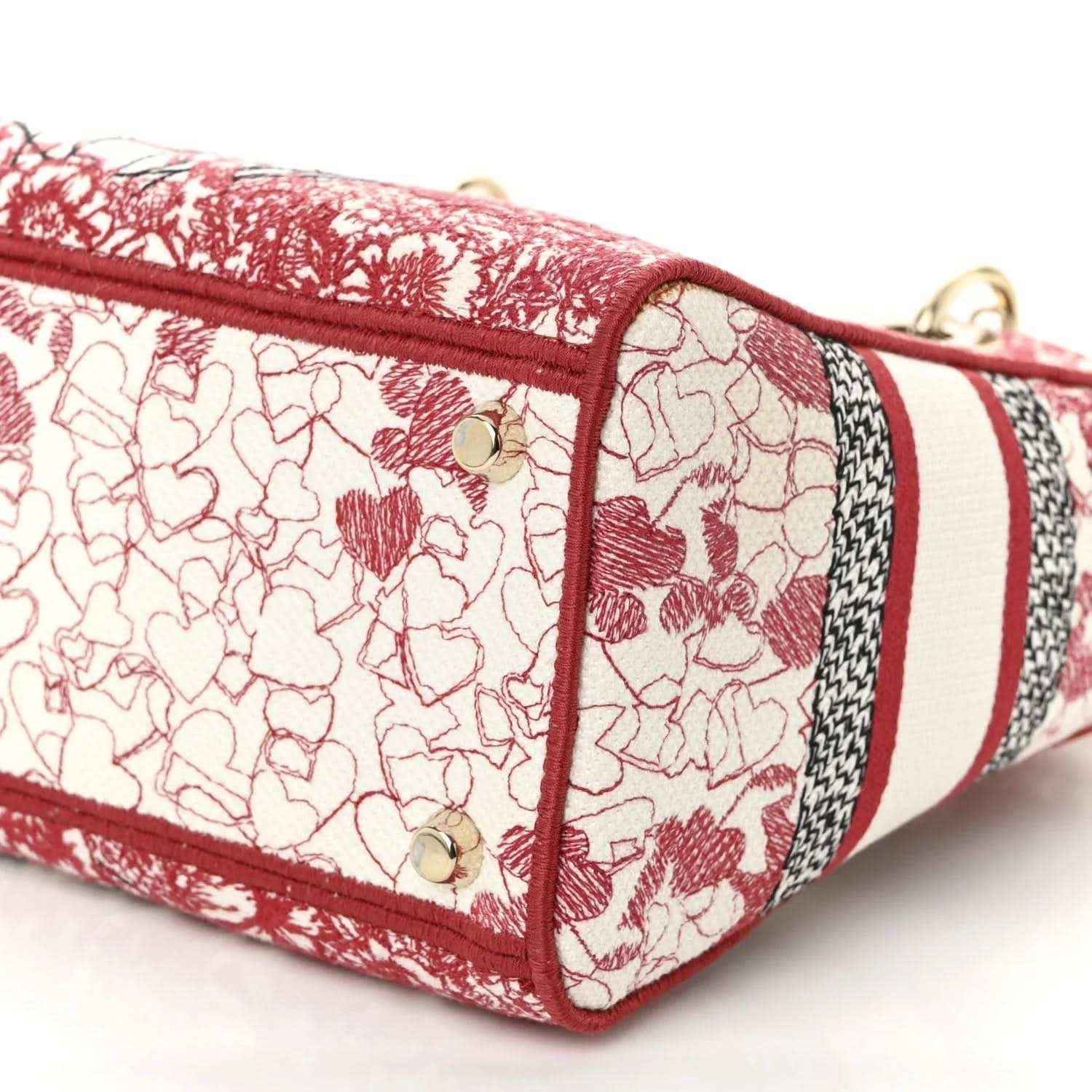Embroidered canvas bag end panel in red-and-white heart pattern with gold studs.