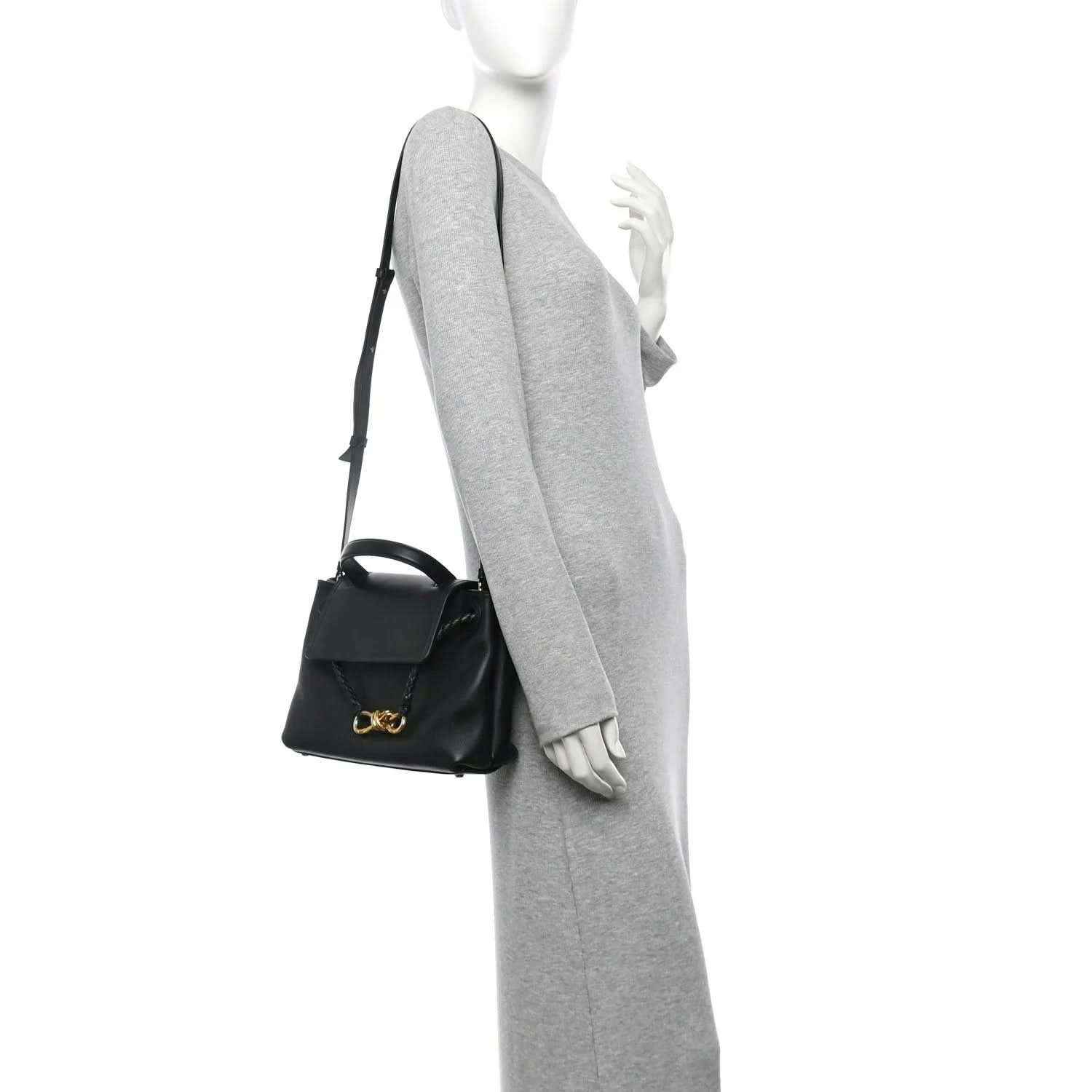 Black small shoulder bag with gold bow clasp, worn crossbody with adjustable strap.