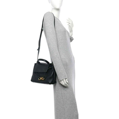 Black small shoulder bag with gold bow clasp, worn crossbody with adjustable strap.