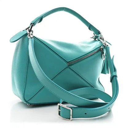 Small Puzzle bag in teal-blue leather with zip top and crossbody strap; side angle.