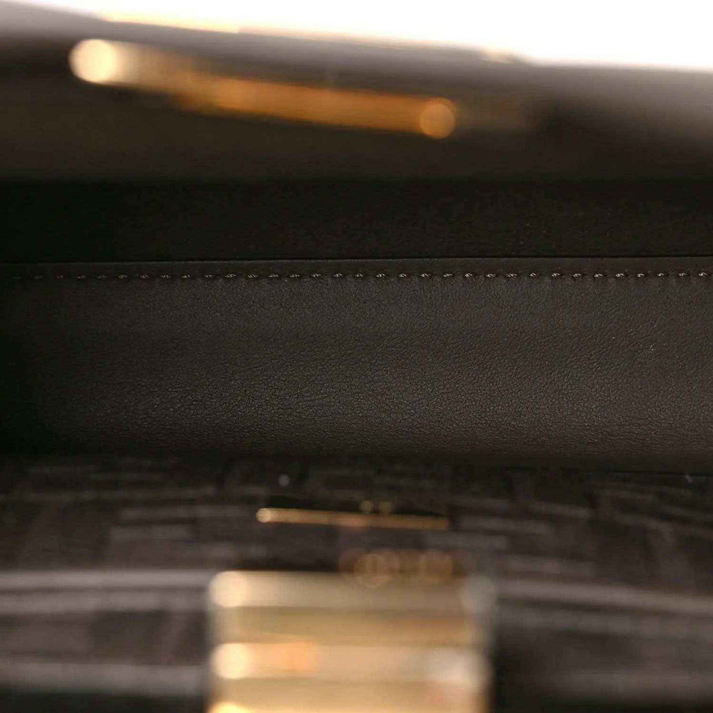 Dark brown leather satchel close-up with stitched seam detail.