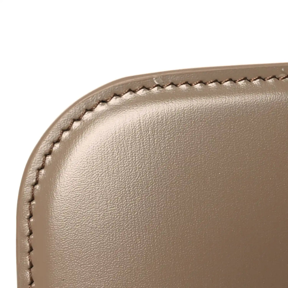 Shiny brown leather bag corner close-up with stitched edge and smooth grain