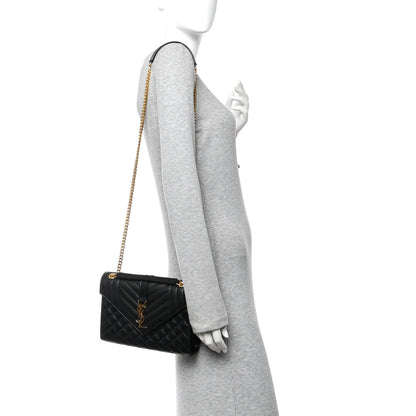 Black quilted mini satchel with flap closure and gold chain shoulder strap on a person