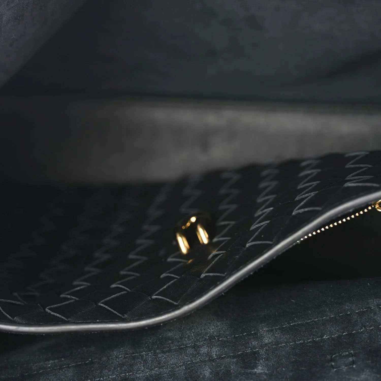 Close-up of black leather interior with patterned lining and gold zipper trim.