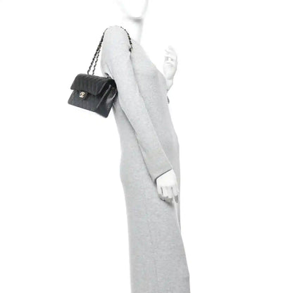 Black leather Chanel small flap bag on a shoulder chain, worn with an overcoat