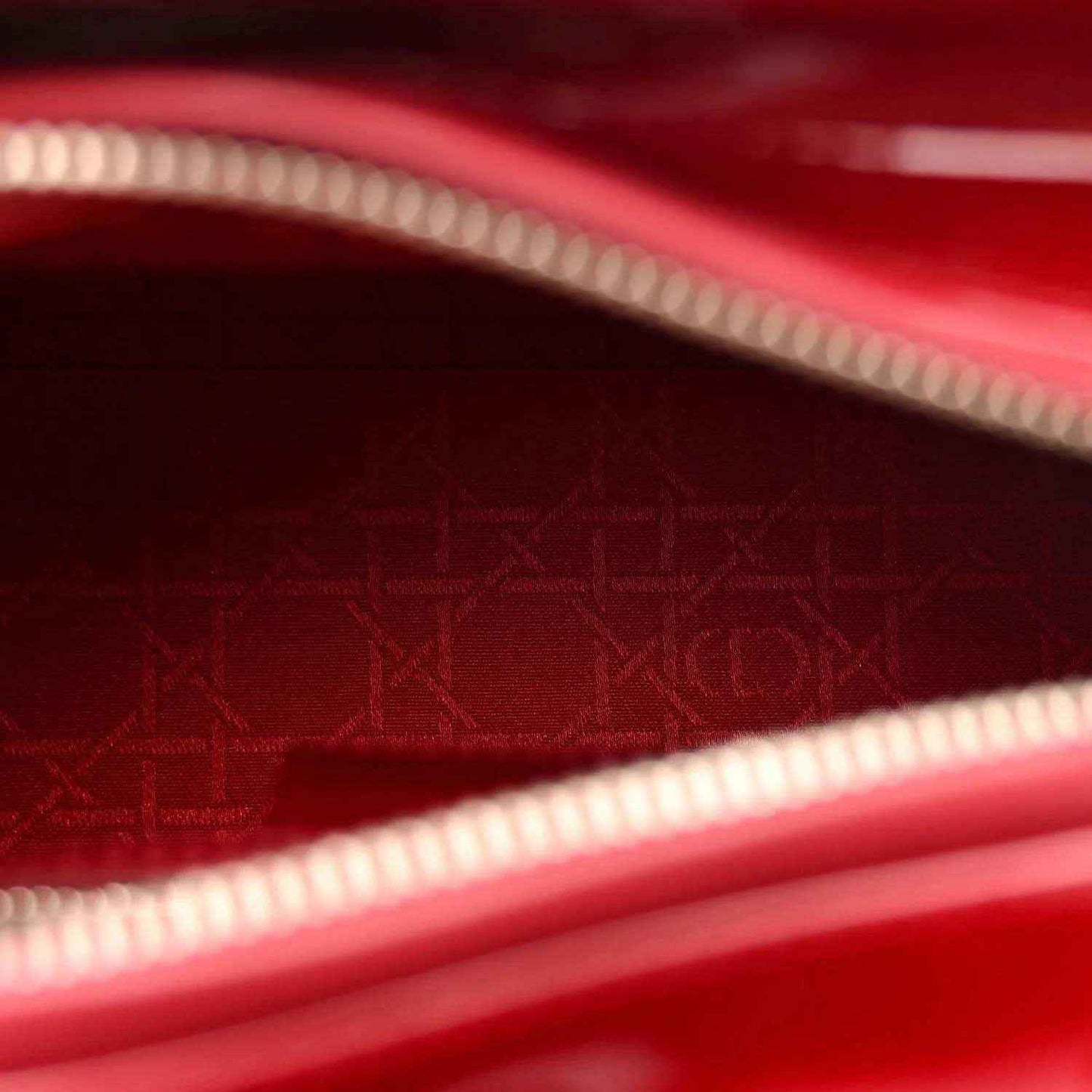 Red patent leather handbag interior lining with monogram pattern and zip trim.