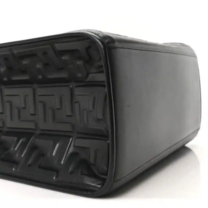Black leather tote bag side view showing embossed interior and smooth exterior panel
