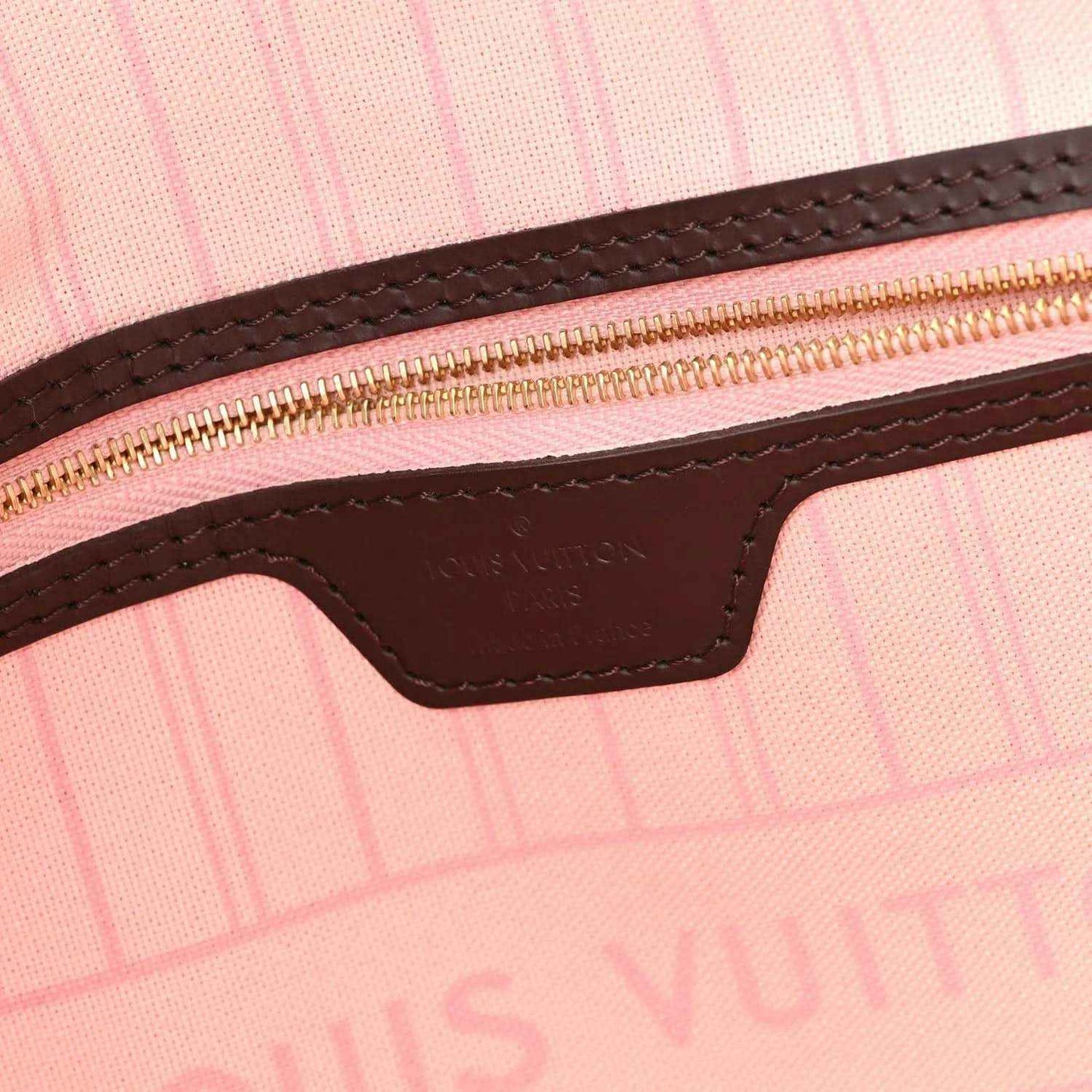 Brown leather zipper tab with gold-tone hardware on pink-lined Neverfull tote