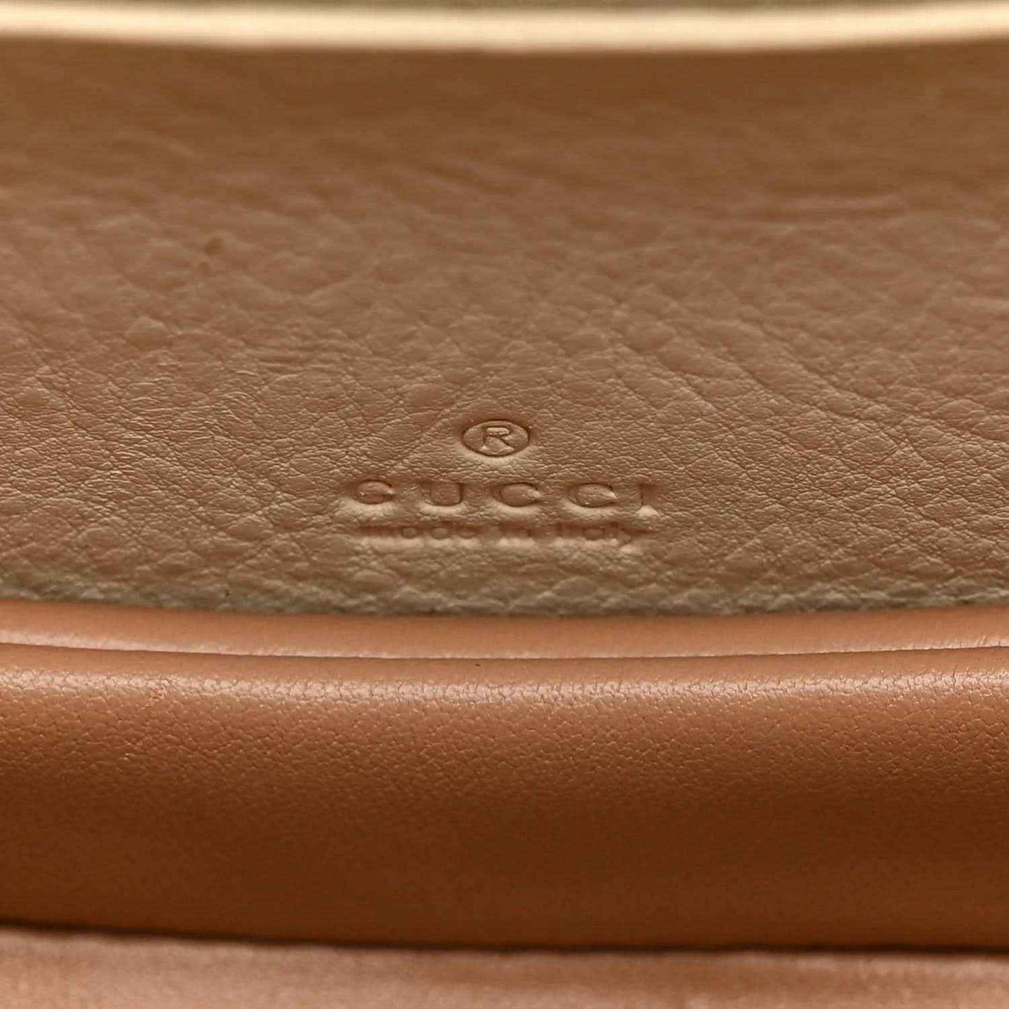 Embossed designer logo on leather base of a white mini handbag