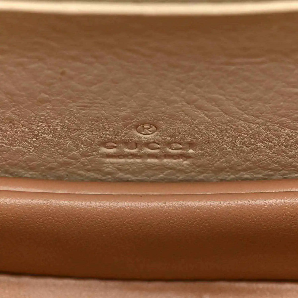 Embossed designer logo on leather base of a white mini handbag