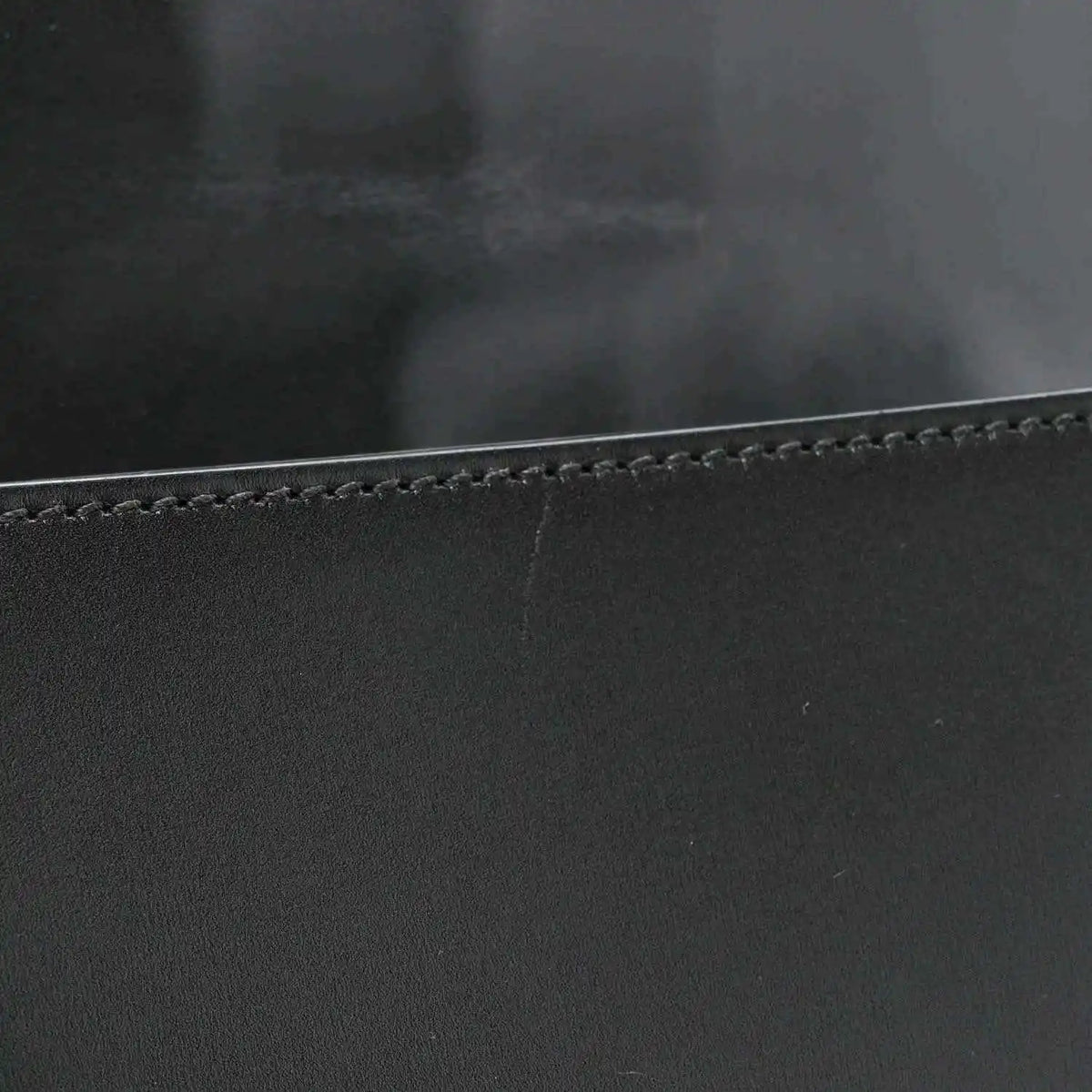 Black leather messenger bag edge with contrast stitching and smooth calfskin texture