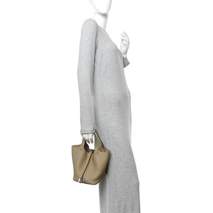 Beige leather tote bag with top handles and front lock closure, carried at side