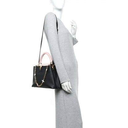 Black leather handbag with pink strap, worn on model arm