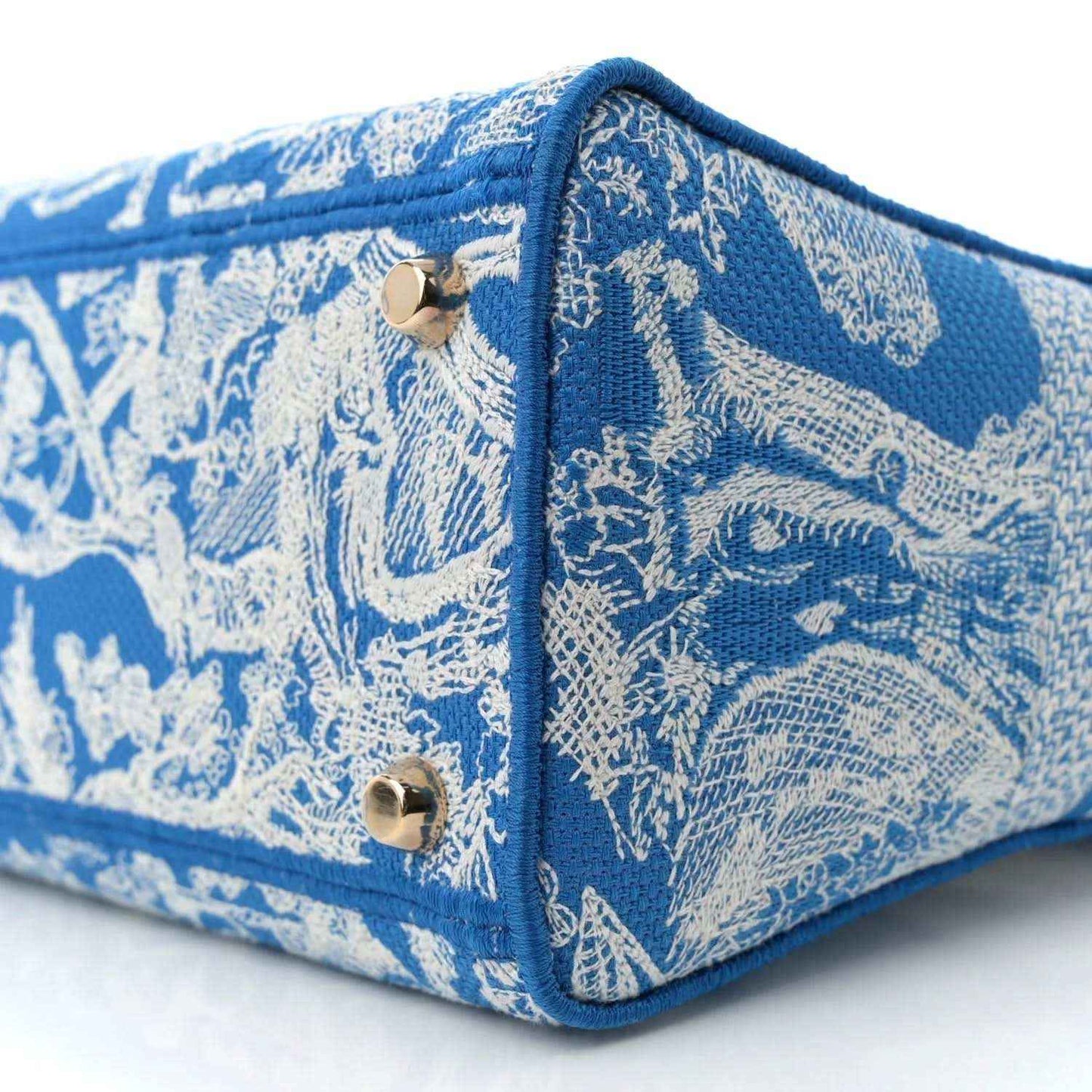 Blue embroidered handbag corner close-up with snap hardware and textured fabric.