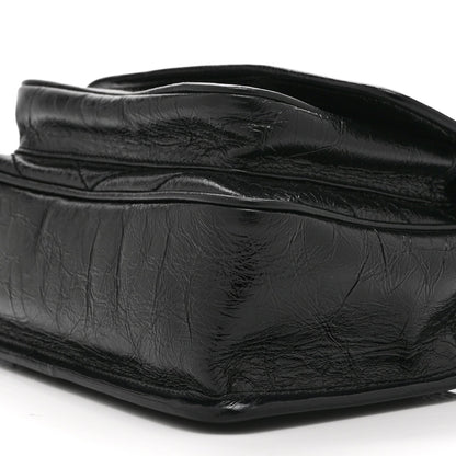 Black leather satchel bag close-up with crinkled finish and curved flap seam