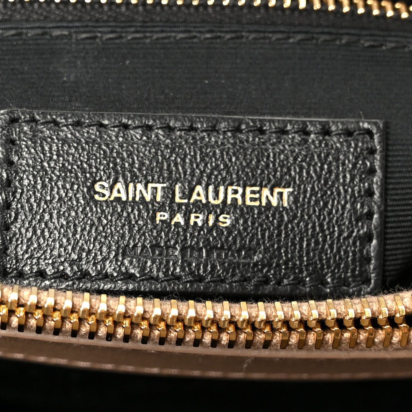 Black leather label with SAINT LAURENT PARIS text and gold zipper