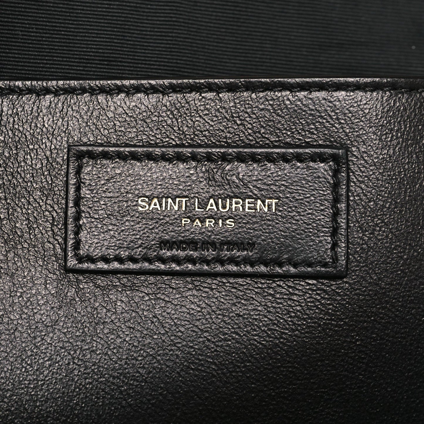 Rectangular leather brand label on bag, stamped text inside border stitching.