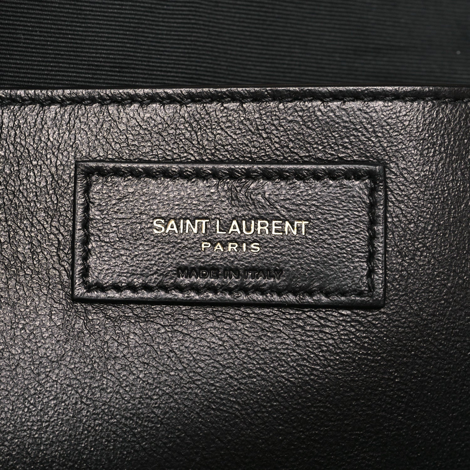 Rectangular leather brand label on bag, stamped text inside border stitching.