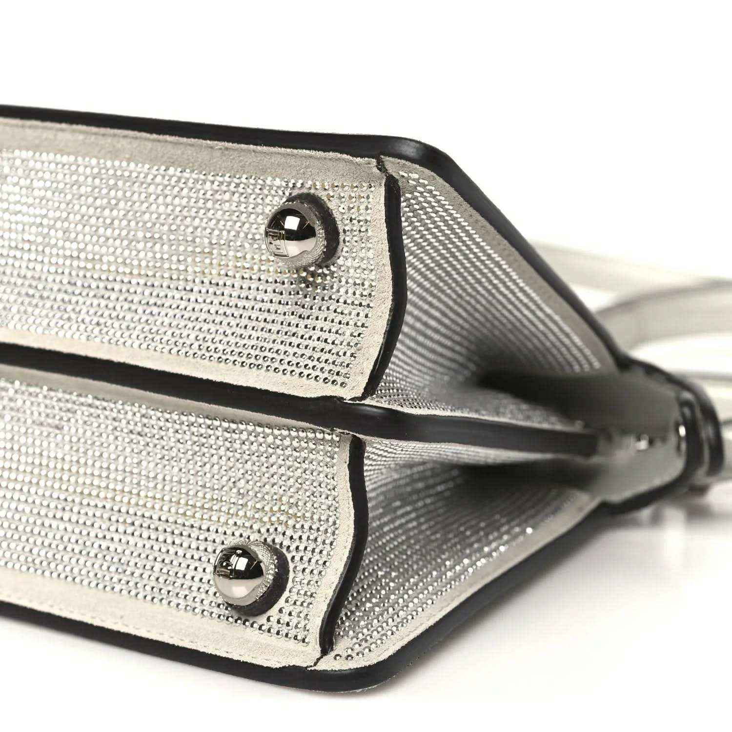 Small satchel bottom edge close-up with rivets, trim piping, and strap attachment